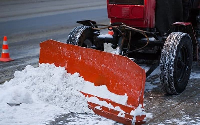 Plow truck fitted with a red snow blade clearing a road during winter