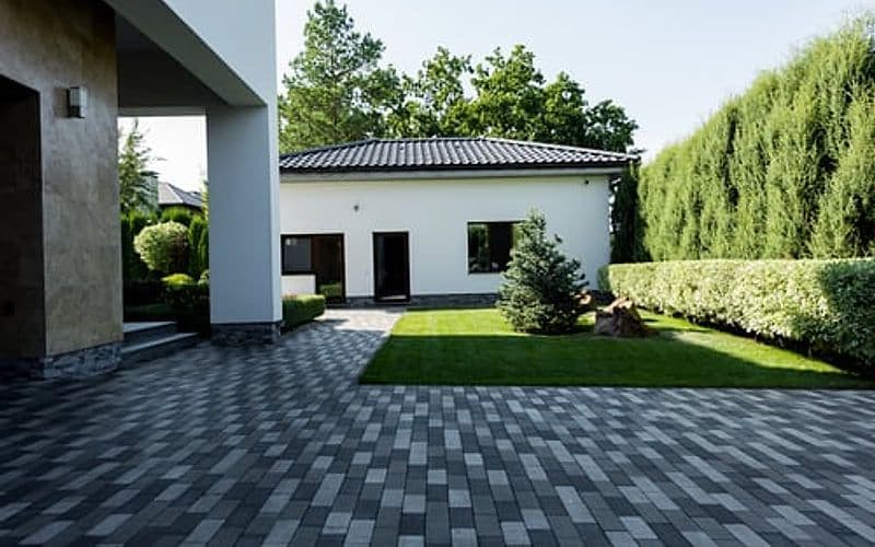 Newly installed paver driveway leading to a modern home with clipped hedging alongside