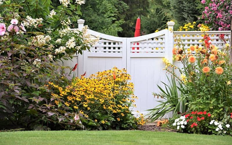 White picket fence bordering a flowering garden bed on a well-kept residential property